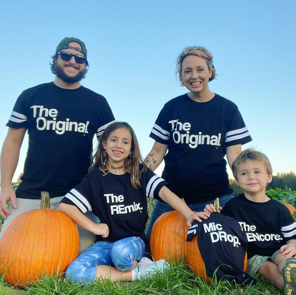 fall pregnancy announcement with matching family shirts showing that a baby is on the way with a baby onesie and cute pumpkins for Fall theme, in the original the remix the encore matching shirts football style shirts with white strips on the sleeves