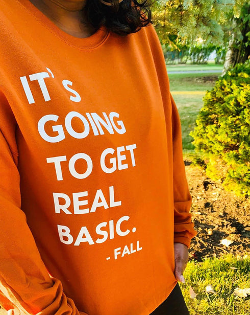 black woman, wearing pumpkin orange sweatshirt about fall with screen print text saying its going to get real basic, fall, soft pullovers