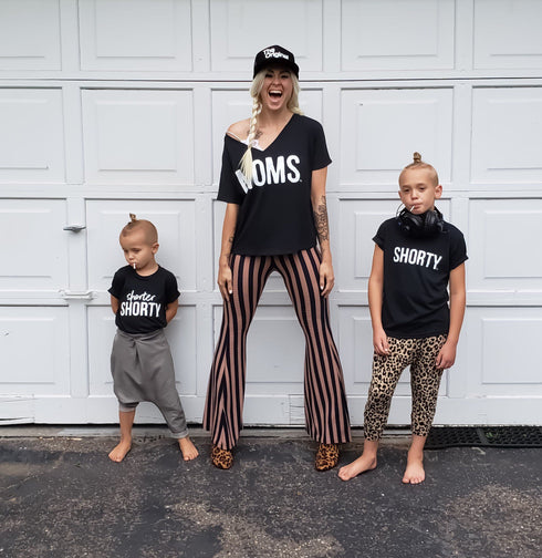 mom and two boys in front of a garage wearing matching shirts with screen print design that says moms shorty and shorter shorty and mom wearing the original hat with a long elsa braid