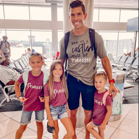 dad matching with three of his daughters wearing an olive shirt by dad that says man of a castle full of princess hashtag girl dad and girls wearing maroon shirts that says princess cute matching shirt set for girl dads